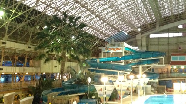 Parque acuático interior con una piscina grande, toboganes de agua y una estructura de techo de paja.