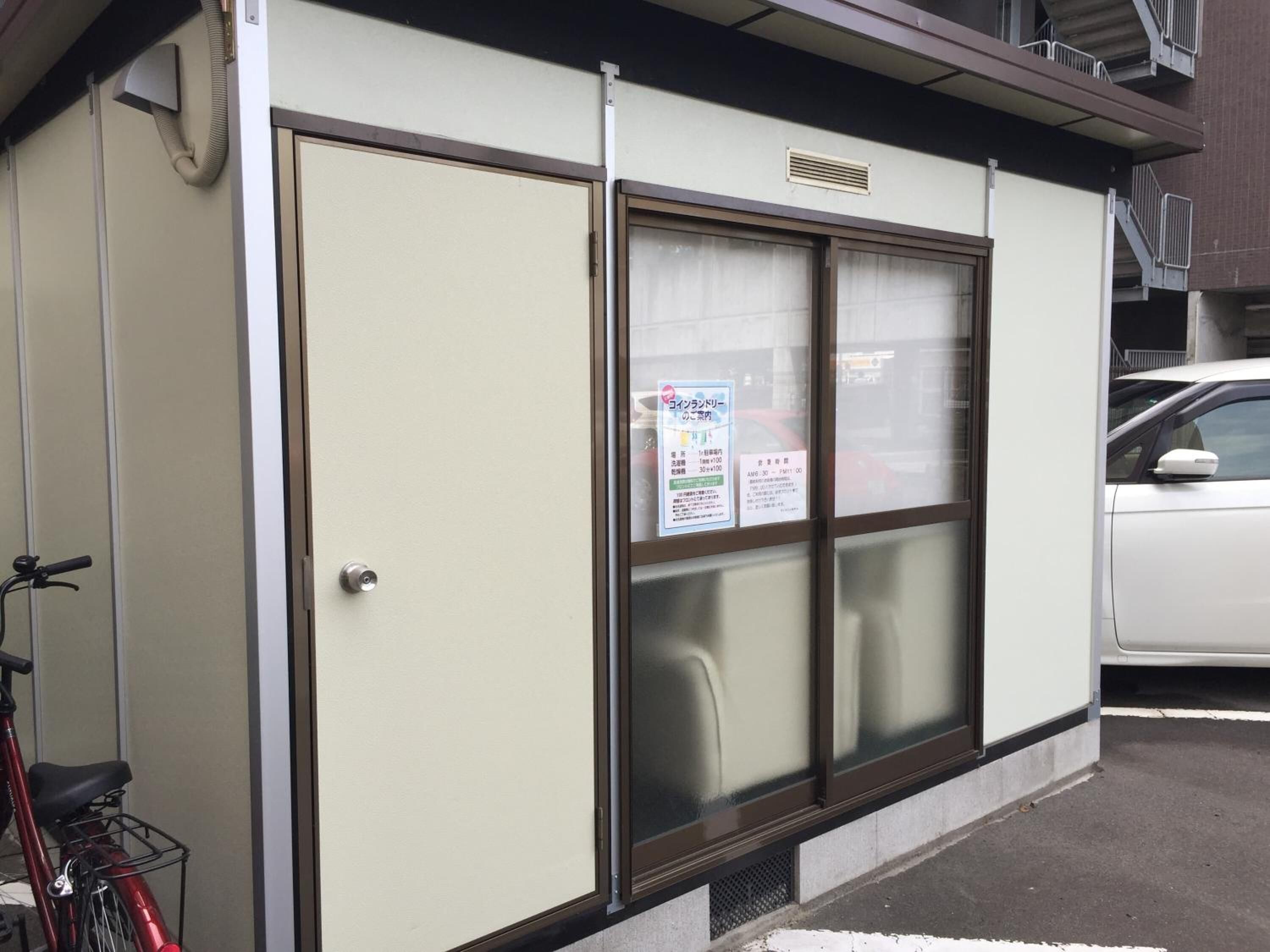 Een gebouw met een grote glazen deur, een fiets voor de deur en een auto op de aangrenzende parkeerplaats.