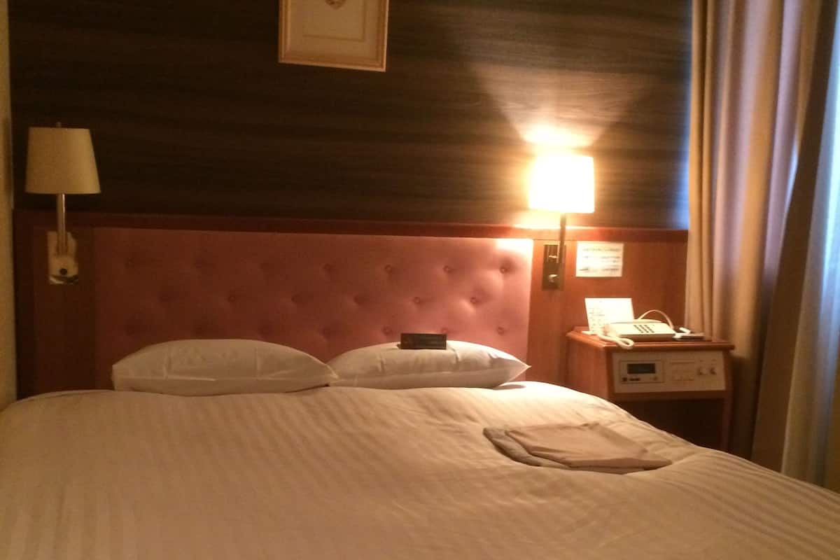 Habitación de hotel con una cama grande, un cabecero, una mesita de noche con lámpara y un teléfono instalado en la pared.