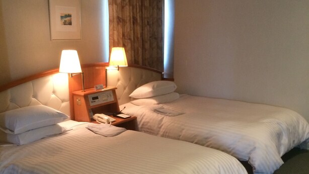 Ein Hotelzimmer mit zwei Einzelbetten, einem Nachttisch mit Lampe, einem Telefon und einem Bild an der Wand.