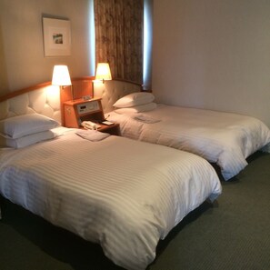 Une chambre d’hôtel avec deux lits simples, une table de chevet avec une lampe, un téléphone et un tableau au mur.