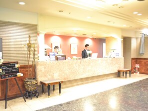 Un espace d’accueil d’hôtel avec un comptoir en marbre, un banc en bois et une plante en pot.