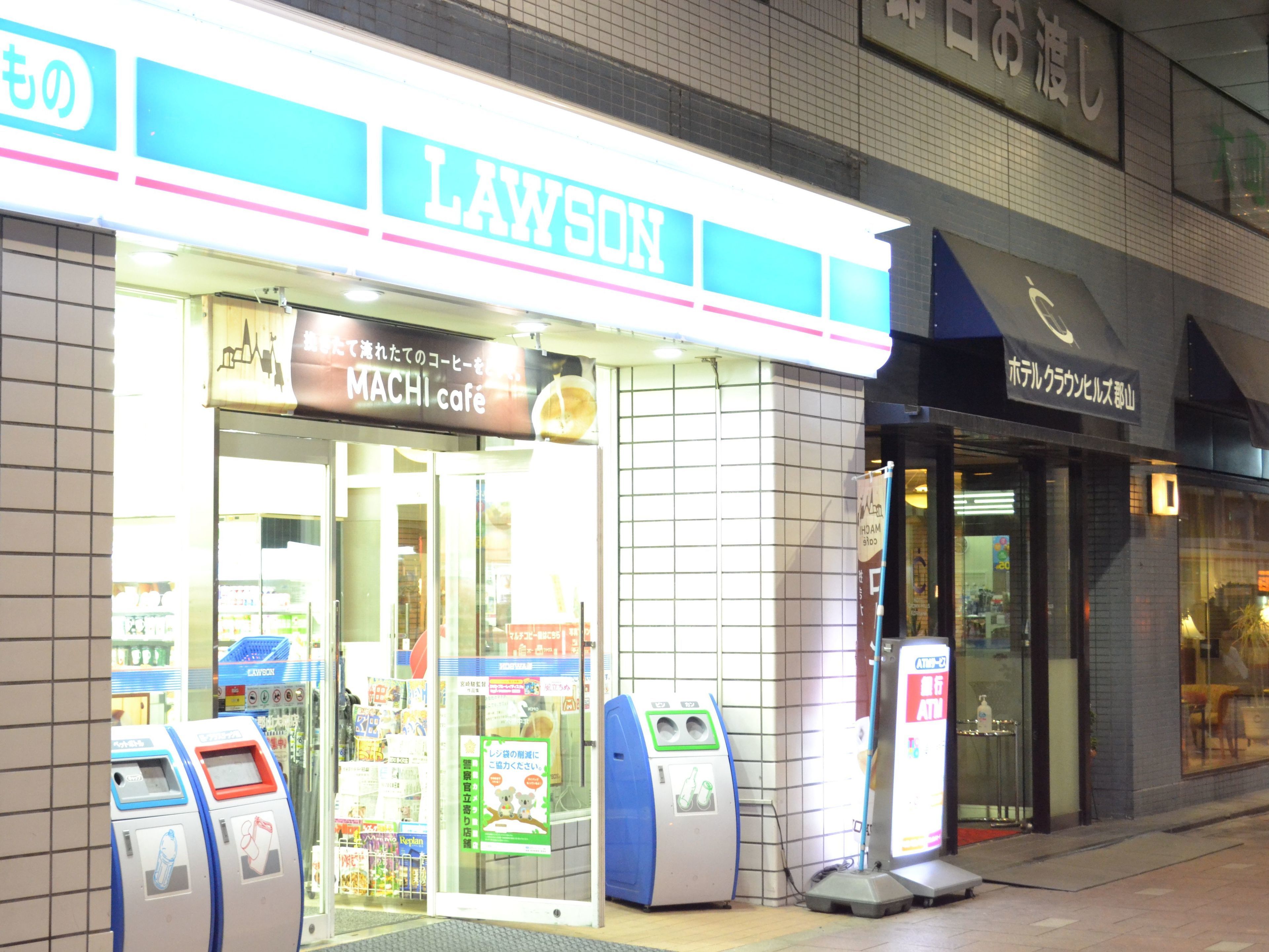 A Lawson store with a bright sign, a MACHI cafe, and ATMs outside.