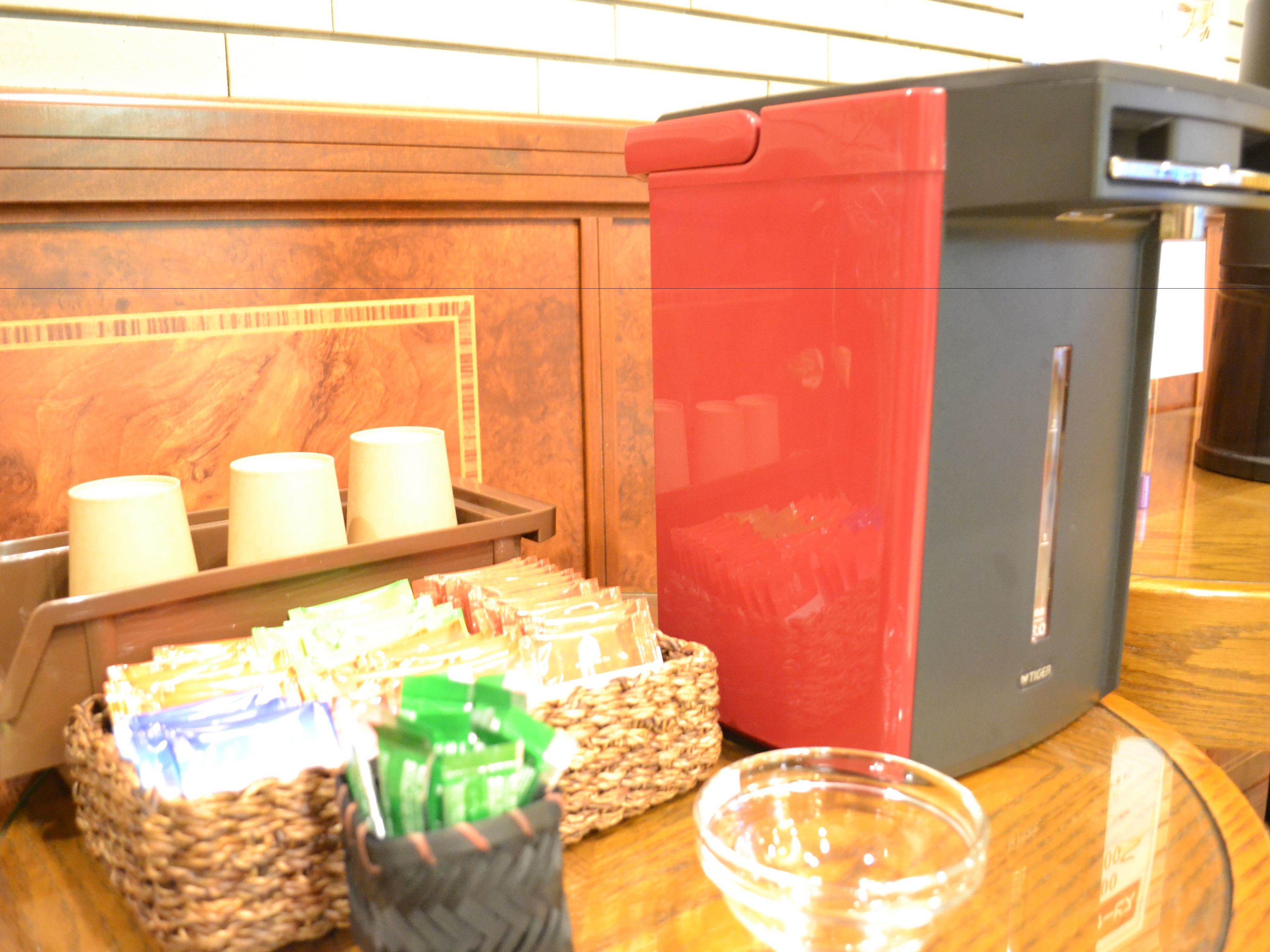 A coffee station with a coffee machine, cups, and a basket of coffee packets.