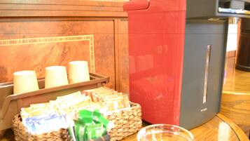 A coffee station with a coffee machine, cups, and a basket of coffee packets.