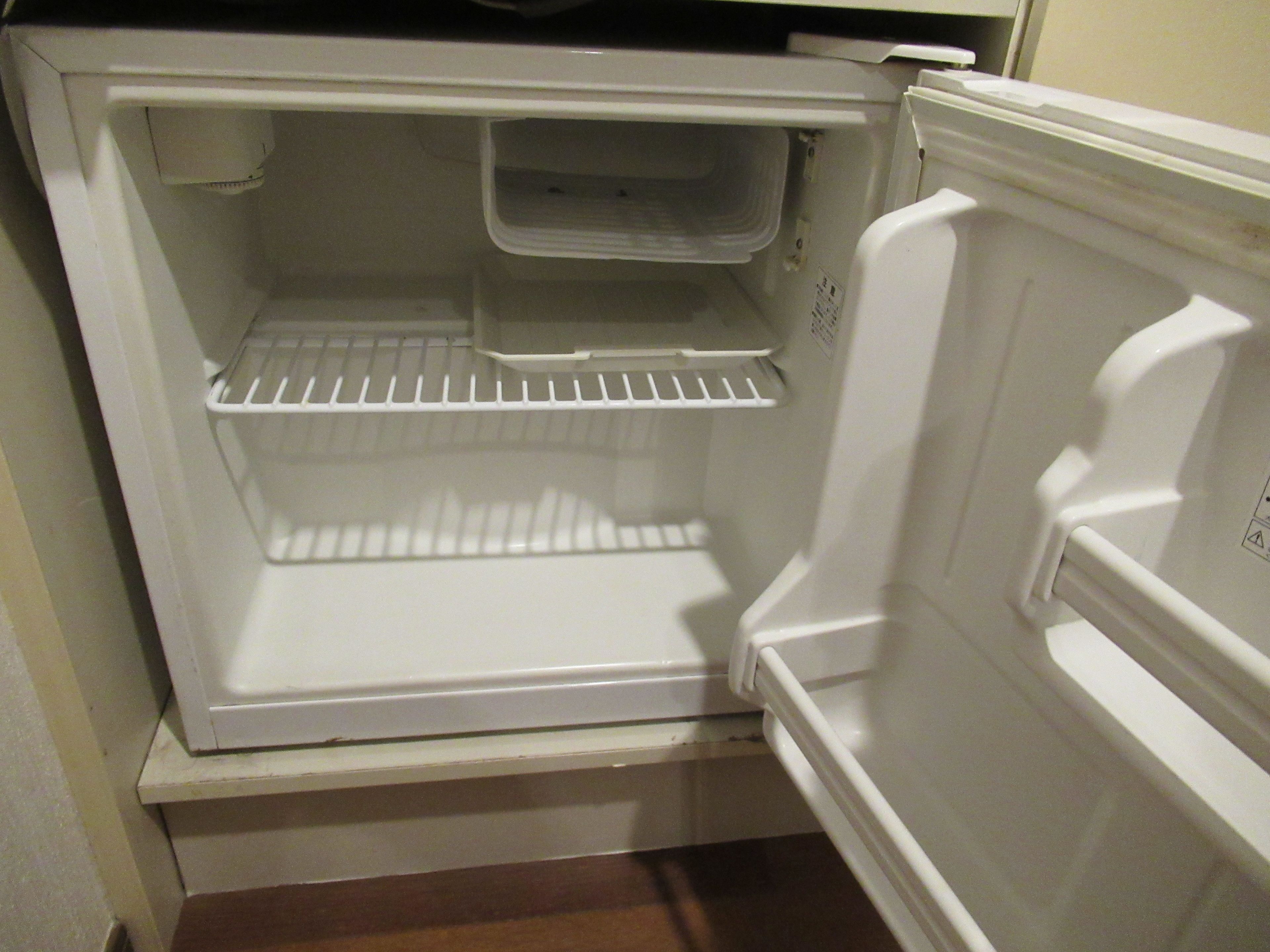 An empty white refrigerator with a shelf and a small compartment.