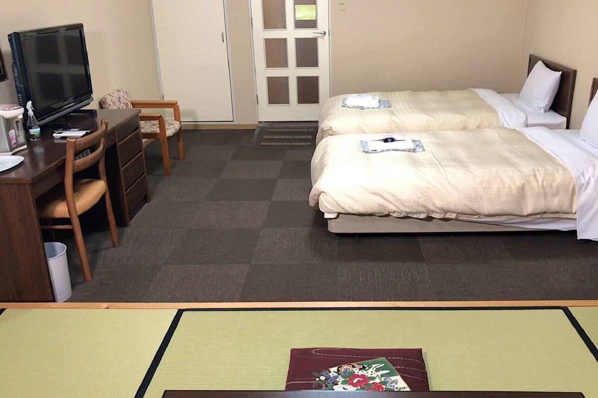 Ein Hotelzimmer mit zwei Betten, einem Schreibtisch, einem Fernseher, einem Sessel und einem kleinen Tisch.