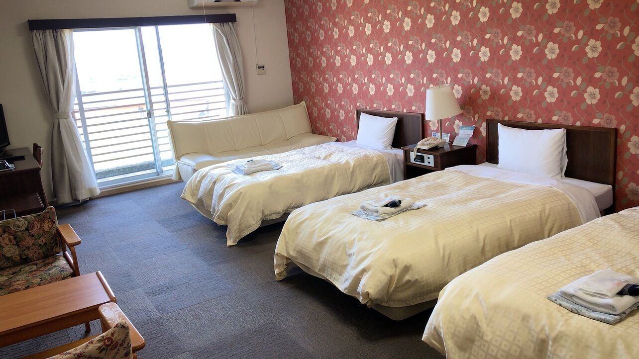 A hotel room with three beds, a sofa, a desk, and a window with curtains.