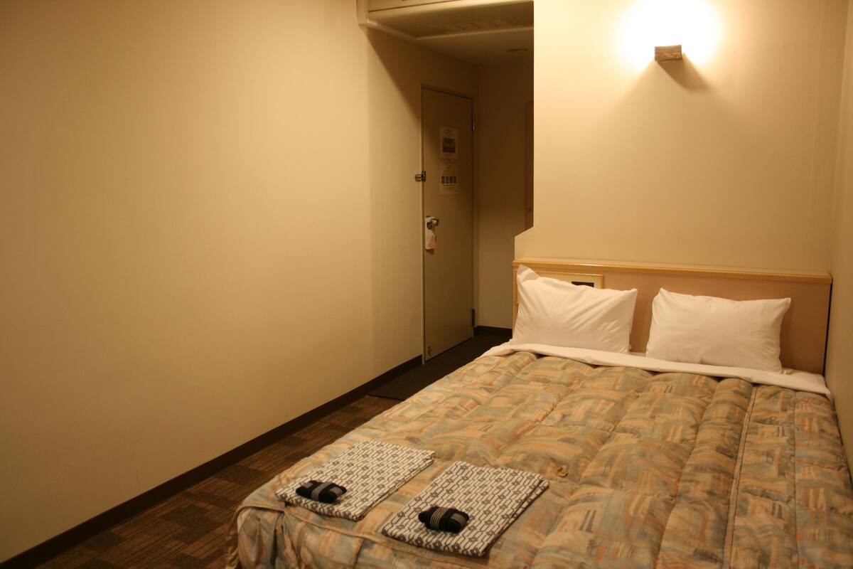 Habitación de hotel con cama, dos almohadas, cabecero, mesita de noche y una puerta.