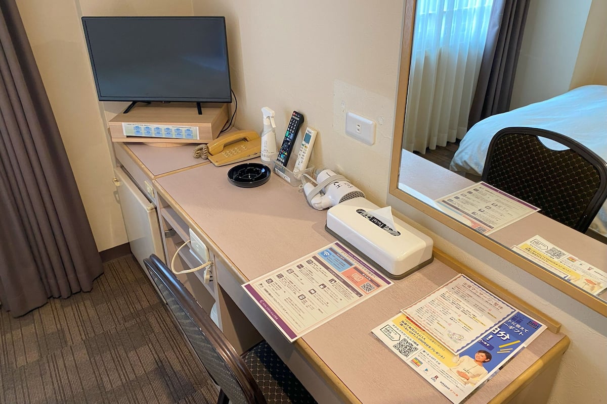 Una habitación de hotel con una cama, un escritorio con teléfono, un espejo y folletos informativos.