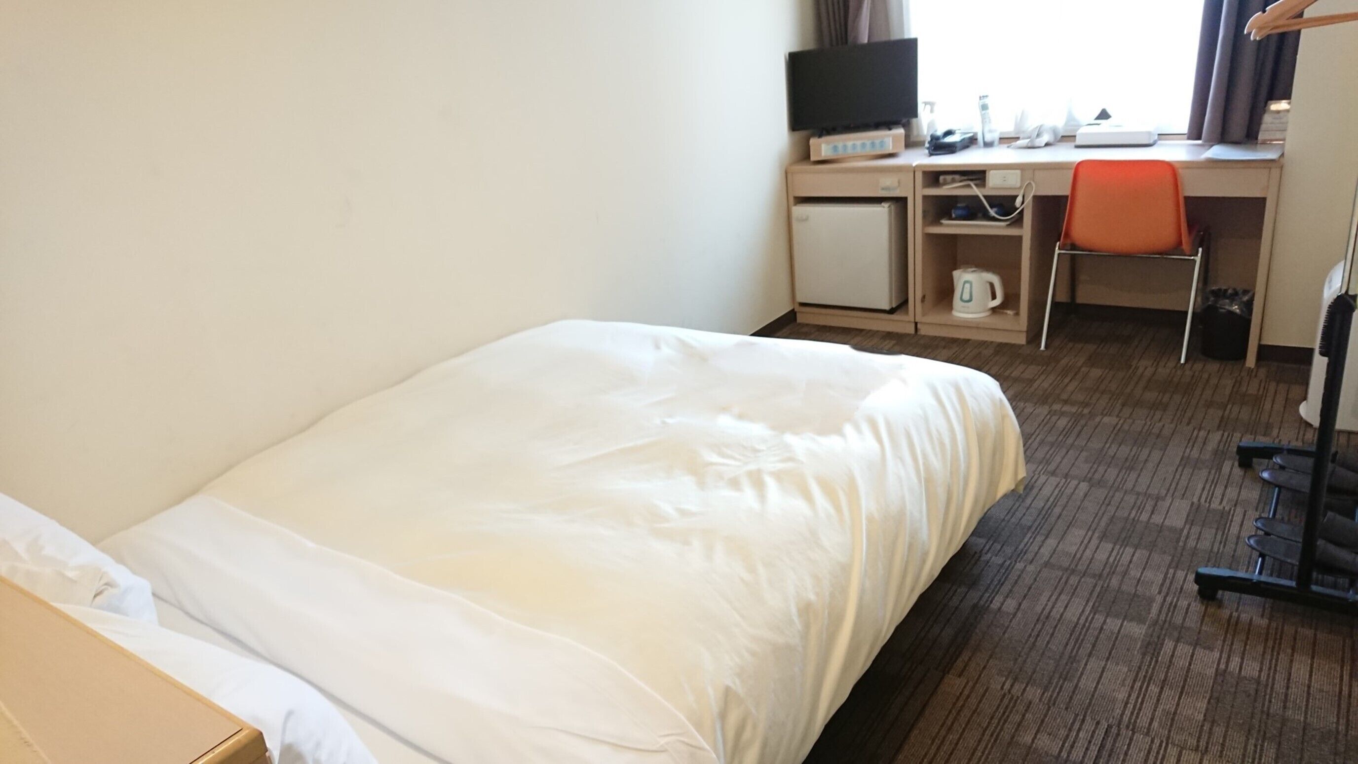 Ein Hotelzimmer mit einem Bett, einem Schreibtisch mit Computer, einem Sessel und einem Fernseher.