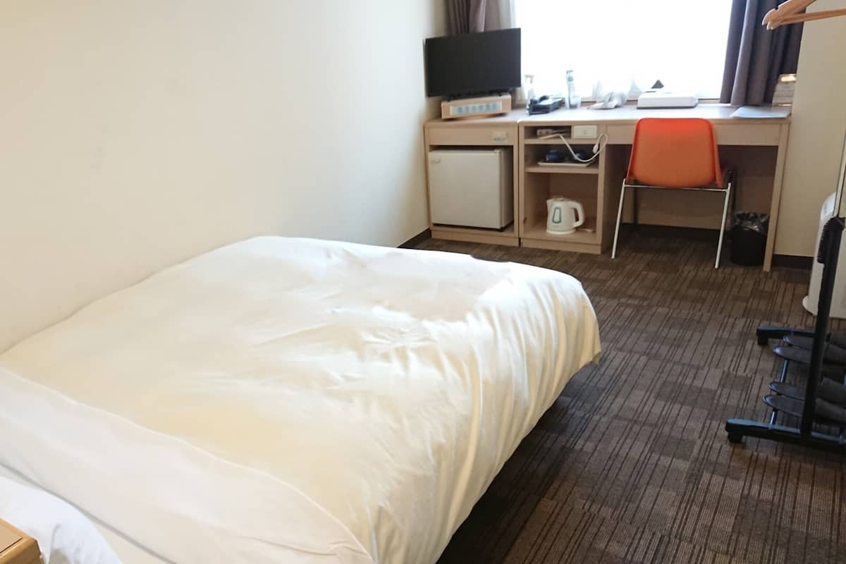 Habitación de hotel con cama, escritorio, computadora, silla y televisor.