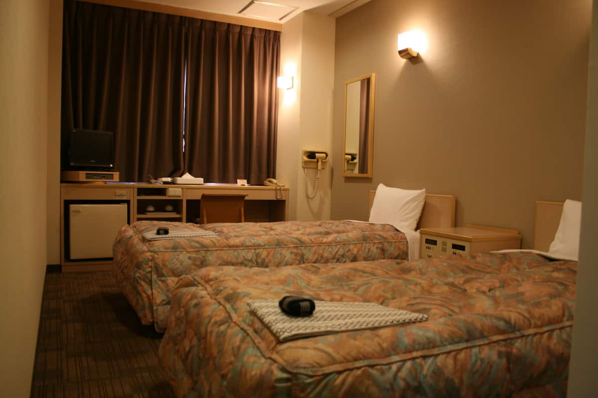 Una habitación de hotel con dos camas, un escritorio con una computadora, un teléfono y un televisor.