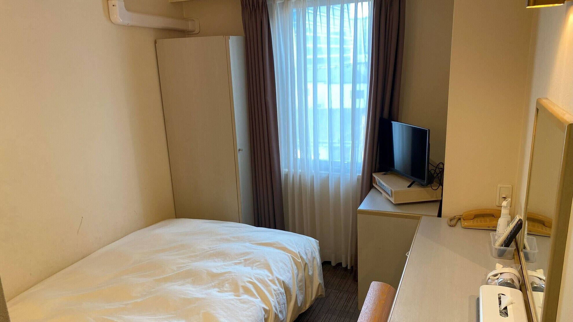 Ein Hotelzimmer mit einem Bett, einem Schreibtisch mit Fernseher, einem Spiegel und einem Telefon.