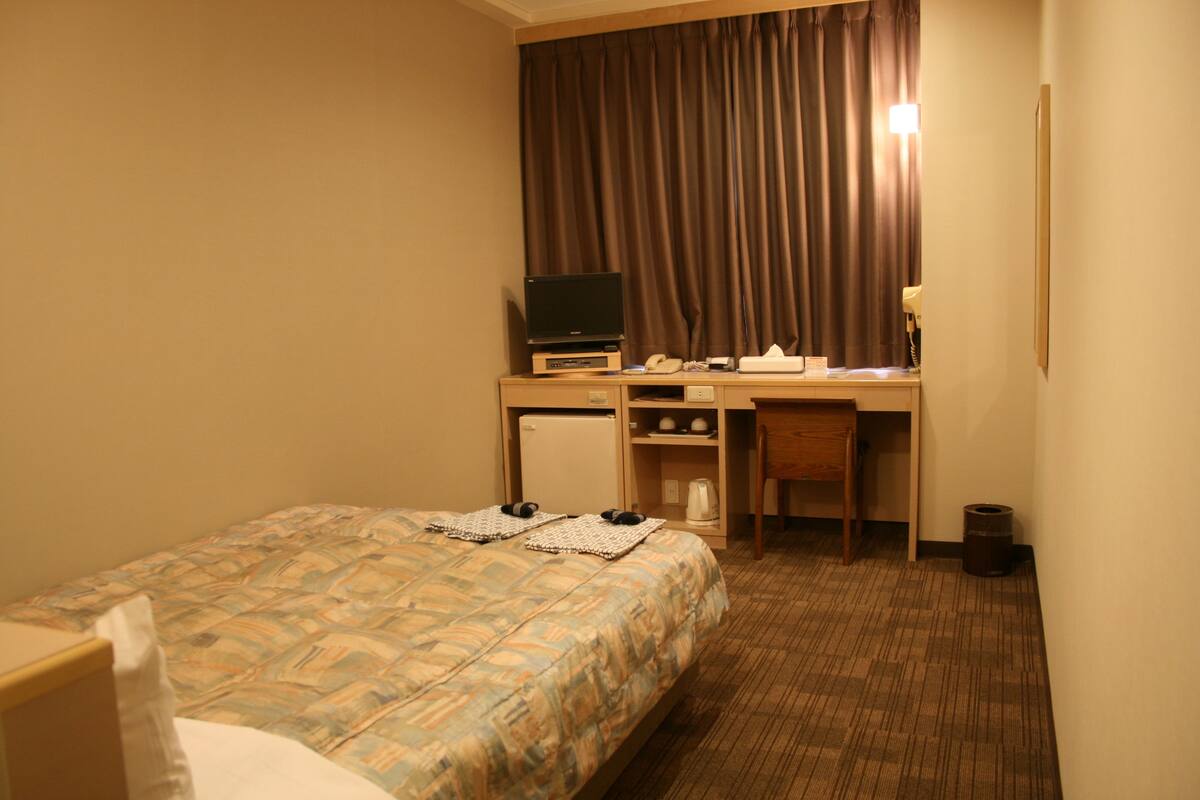 Una habitación de hotel con una cama, un escritorio, una silla, un televisor y un refrigerador pequeño.