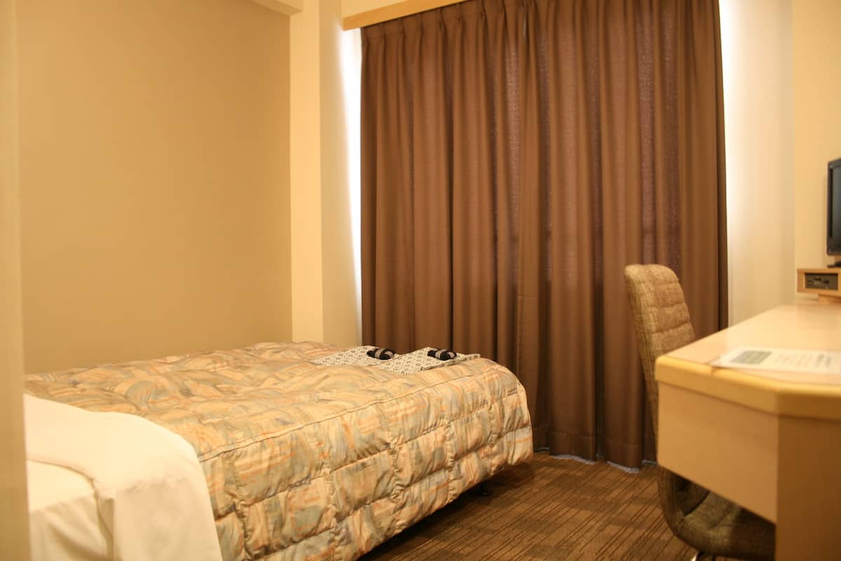 Una habitación de hotel con cama, escritorio, silla y televisión.