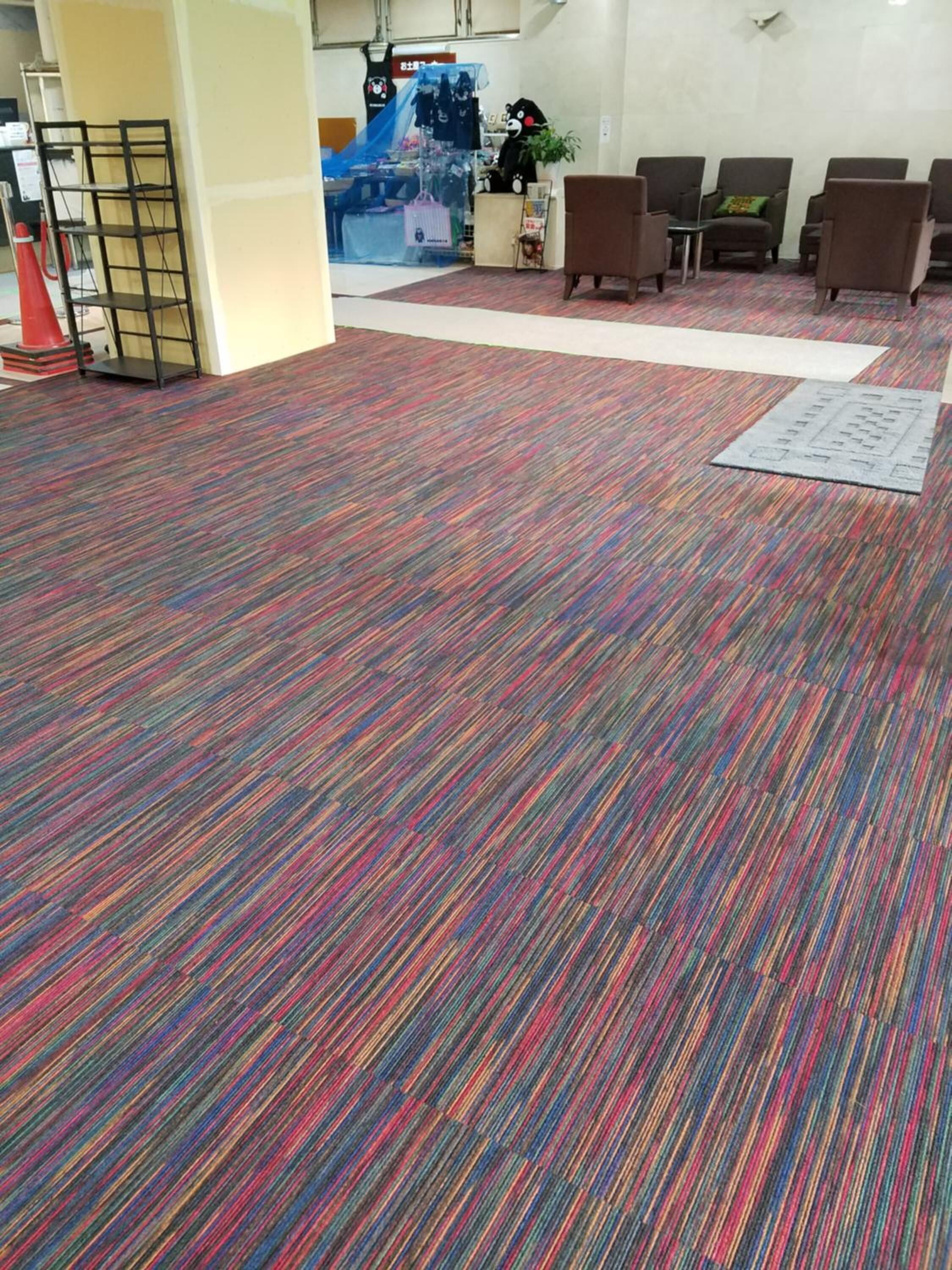 A carpeted lobby with a patterned floor, a reception area with a counter and a plush toy, and several seating areas.