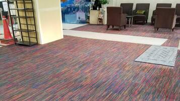 A carpeted lobby with a patterned floor, a reception area with a counter and a plush toy, and several seating areas.