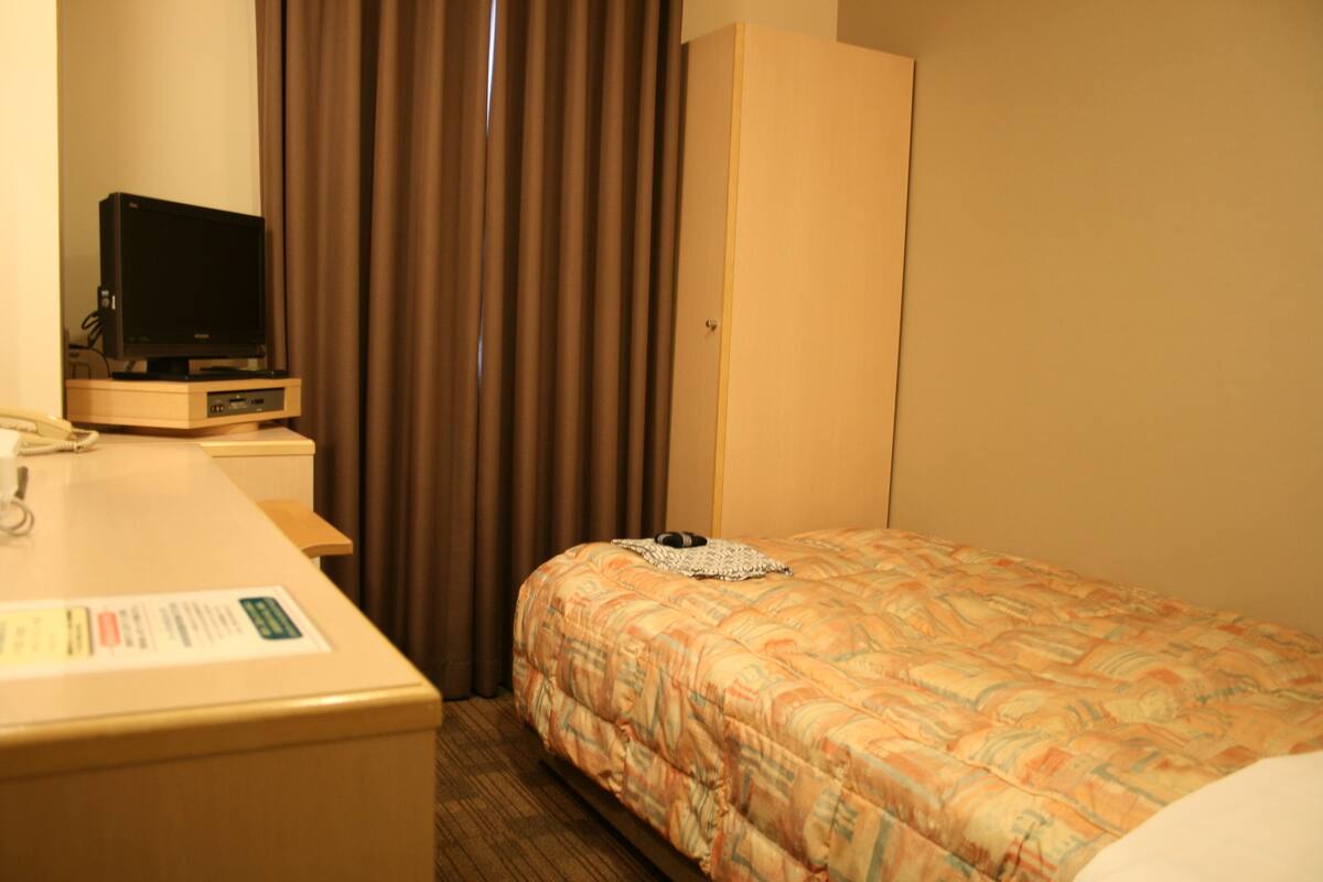 Una habitación de hotel con cama, escritorio con televisor y armario.