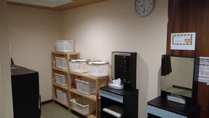 A room with a wooden shelf holding white laundry baskets, a black cabinet, a mirror, and a clock on the wall.