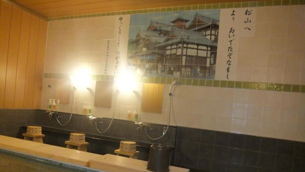 A traditional Japanese-style bathroom with a wooden floor, a long bench, and a large mirror.