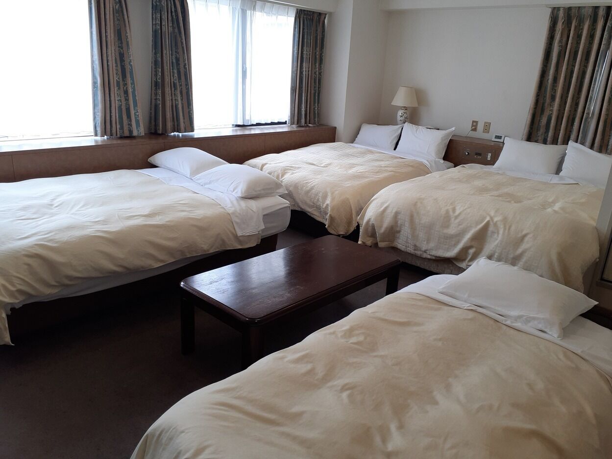 Una habitación de hotel con tres camas, una mesita de noche de madera y una ventana con cortinas.