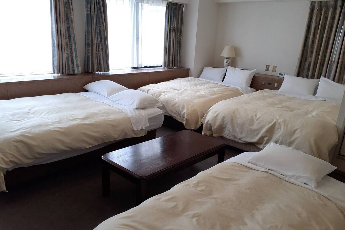 Una habitación de hotel con tres camas, una mesita de noche de madera y una ventana con cortinas.