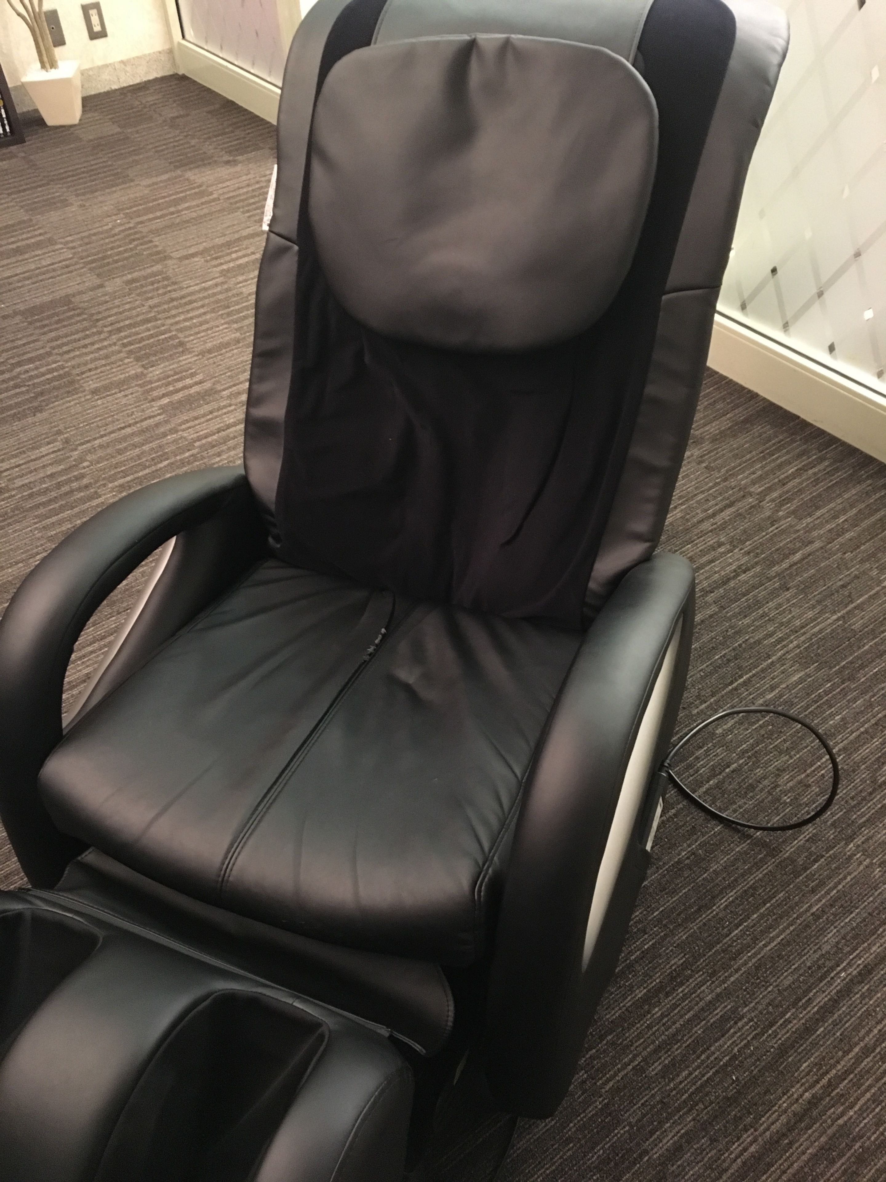 A massage chair with a headrest and footrest, positioned on a carpeted floor.