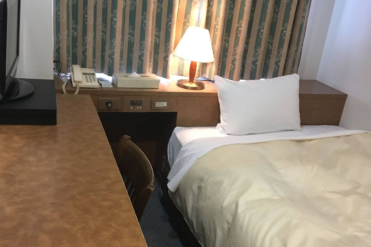 Ein Hotelzimmer mit Bett, Schreibtisch, Telefon, Lampe und Stuhl.