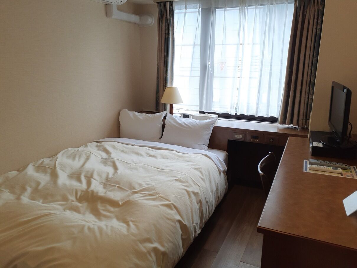 Una habitación de hotel con cama, escritorio, silla, lámpara y televisión.