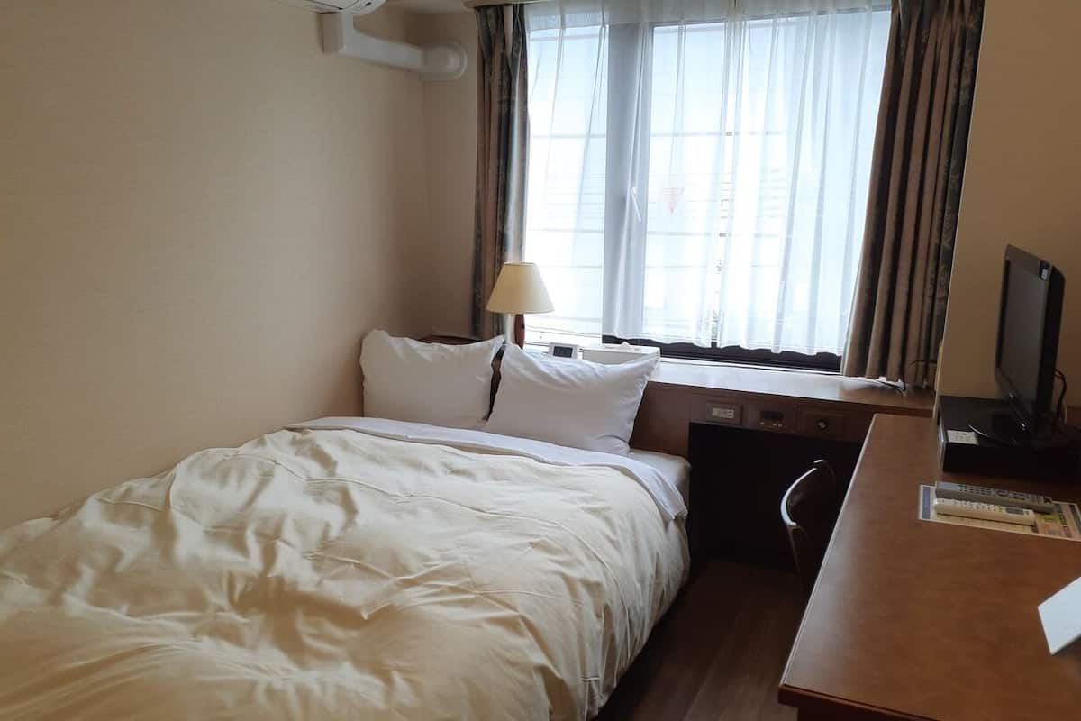 Una habitación de hotel con cama, escritorio, silla, lámpara y televisión.