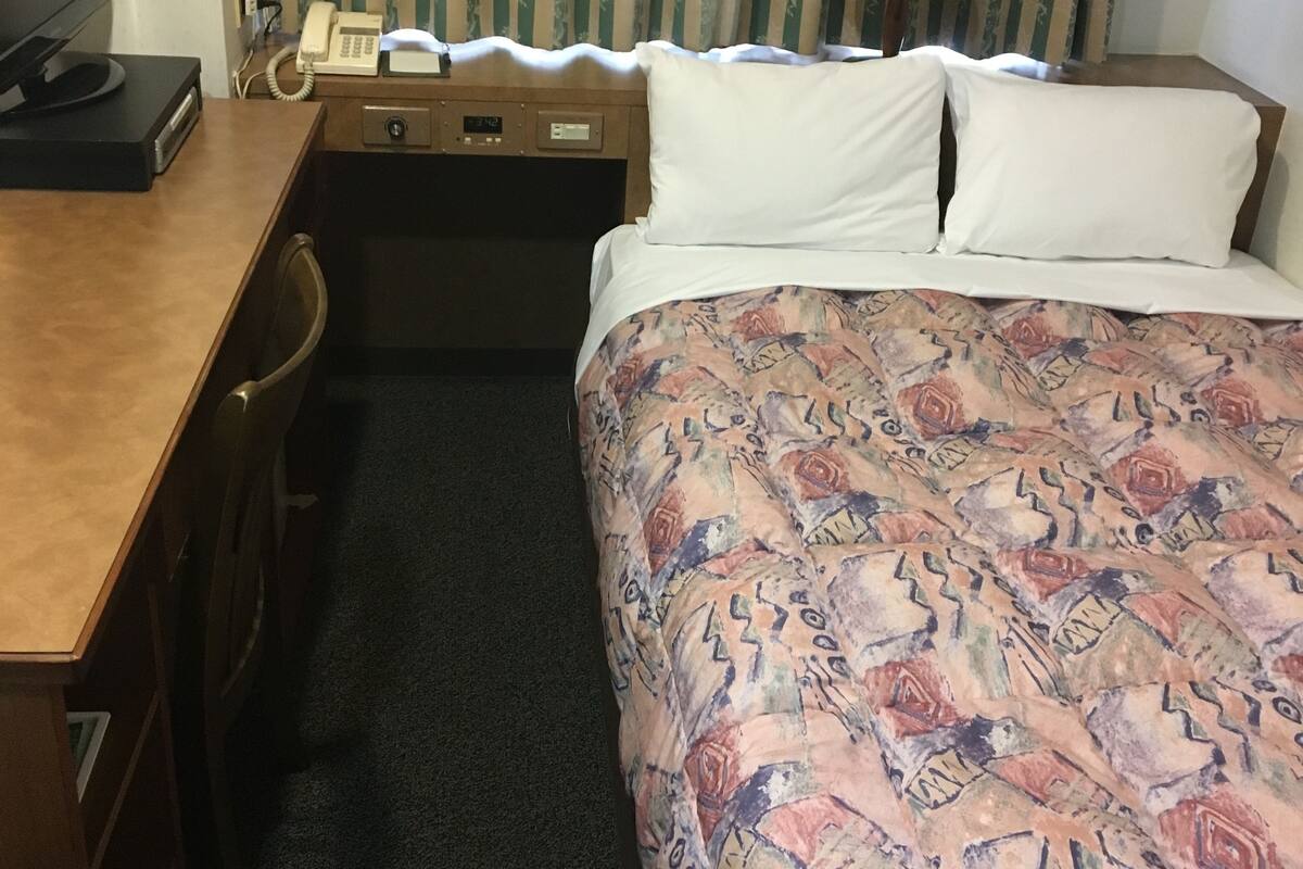 Ein Hotelzimmer mit einem Bett, einem Schreibtisch mit Telefon, einem Fernseher und einer Lampe.