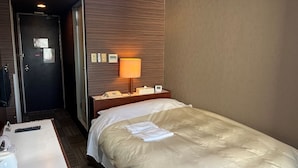 A hotel room with a bed, a bedside table, a lamp, a phone, and a door.