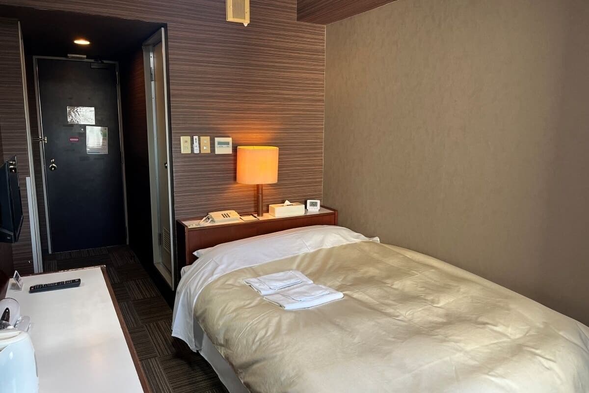 Une chambre d’hôtel avec un lit, une table de chevet, une lampe, un téléphone et une porte.