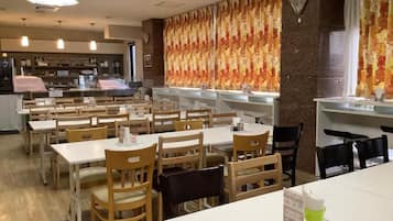 Een restaurant met meerdere tafels en stoelen, een toonbank met een menukaart, en een behangen muur.
