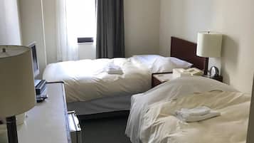 A hotel room with two beds, a desk with a lamp, a telephone, and a window with curtains.