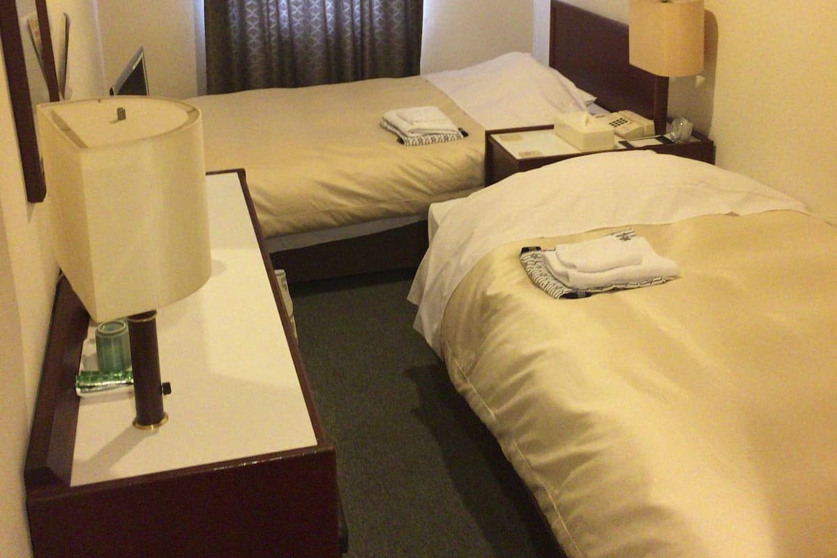 Une chambre d’hôtel avec deux lits, un bureau avec une lampe, un téléphone et une fenêtre avec des rideaux.