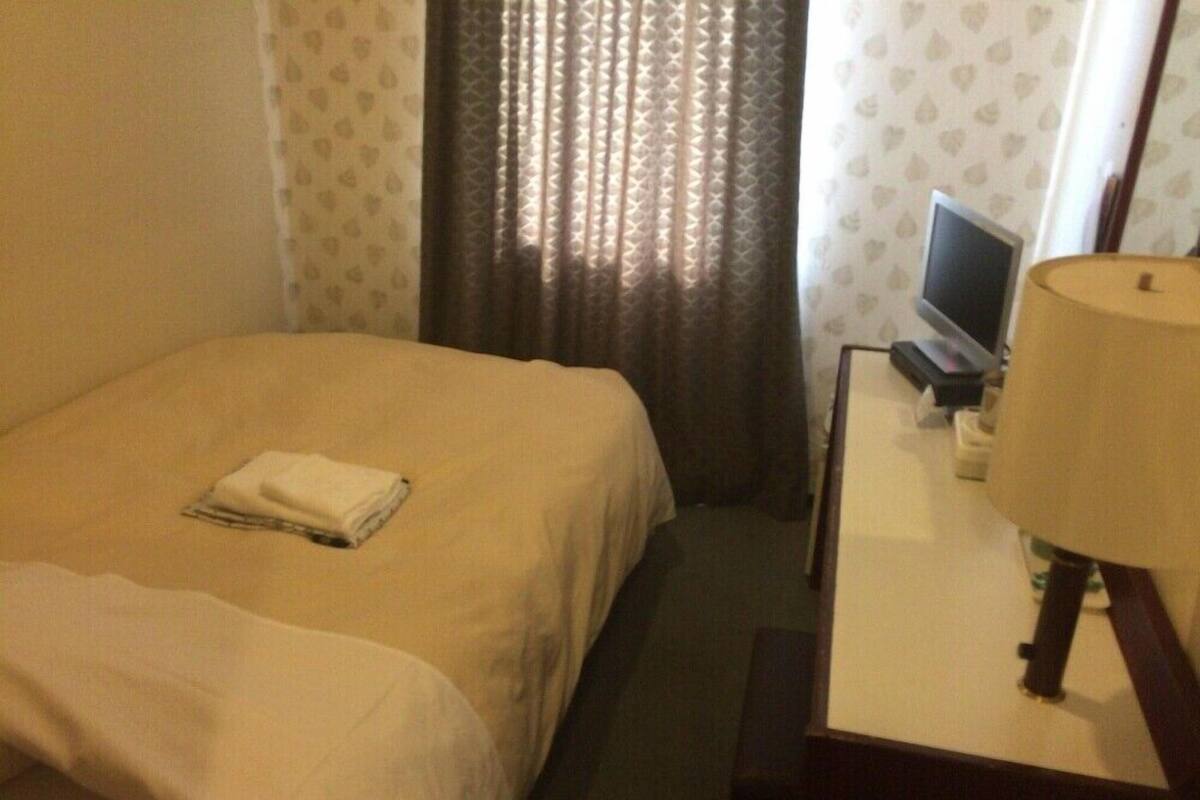Une chambre d’hôtel avec un lit, un bureau avec une lampe, une télévision et des rideaux.
