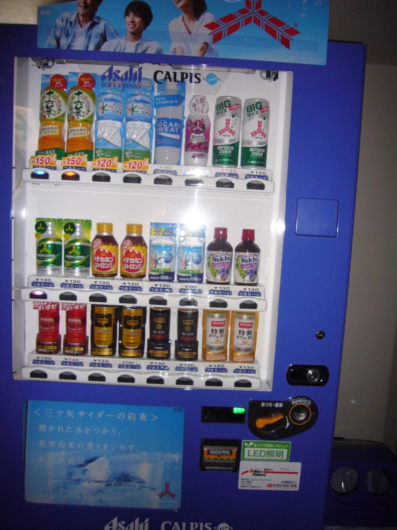 Máquina expendedora con diversas bebidas y aperitivos, incluyendo Calpis, Welch's y otras marcas, con precios indicados en yenes.