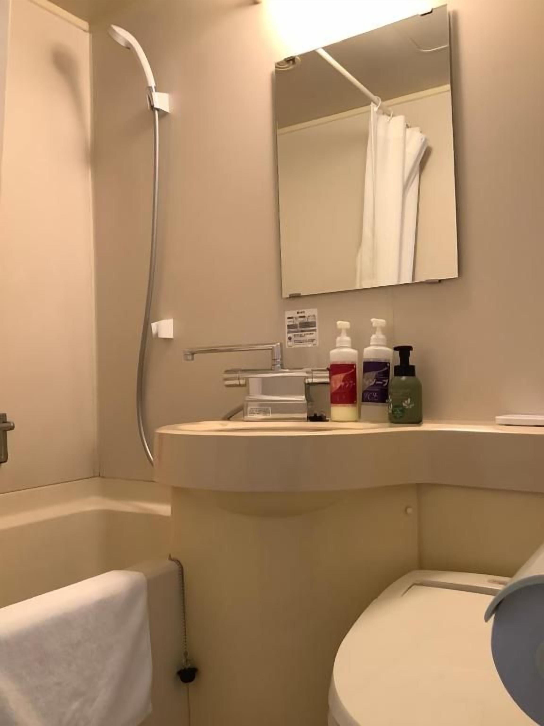 A bathroom with a bathtub, a toilet, a sink with toiletries, and a mirror.