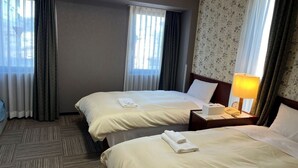Une chambre d’hôtel avec deux lits, une table de chevet avec une lampe et une fenêtre avec des rideaux.
