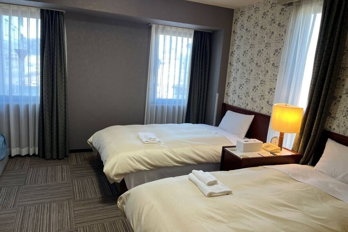 Une chambre d’hôtel avec deux lits, une table de chevet avec une lampe et une fenêtre avec des rideaux.