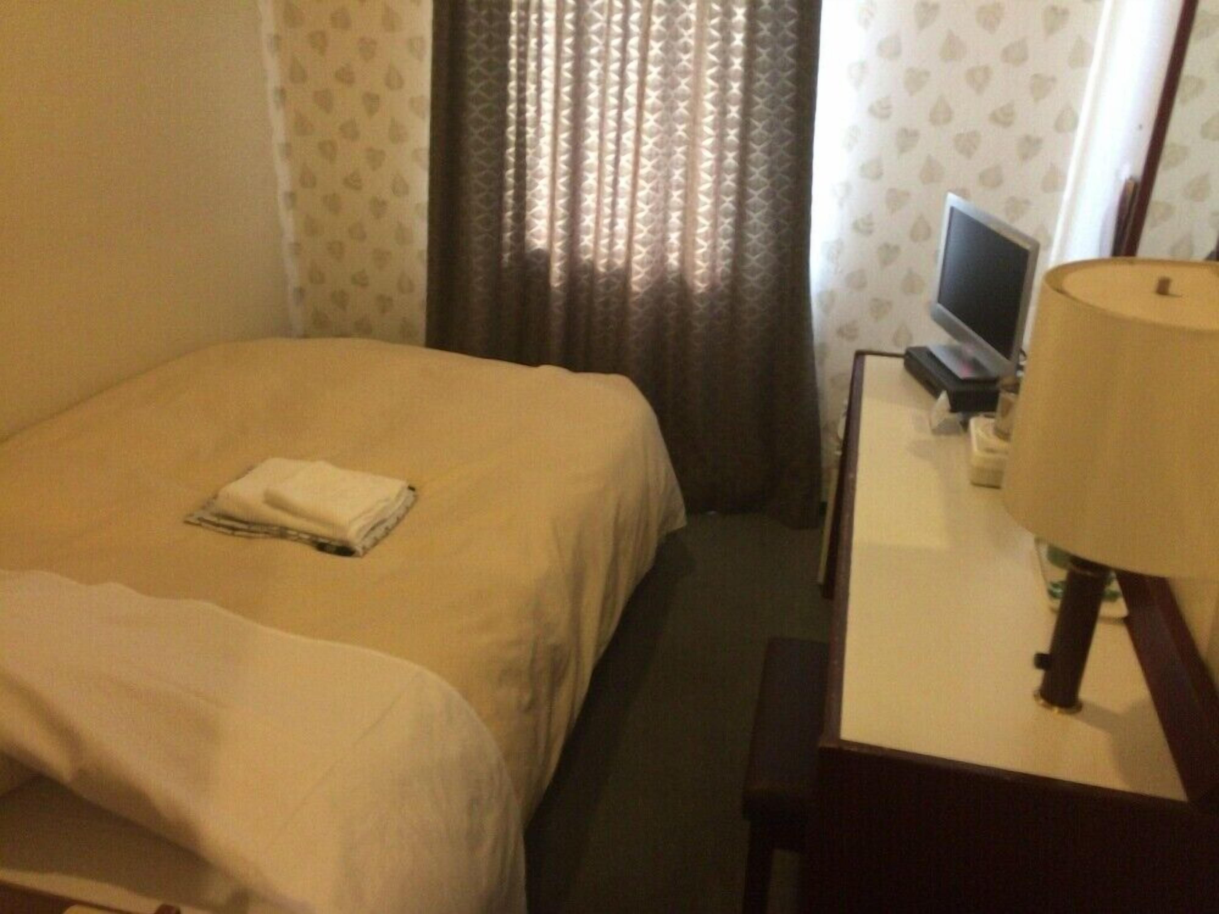 Une chambre d’hôtel avec un lit, un bureau avec une lampe, une télévision et des rideaux.