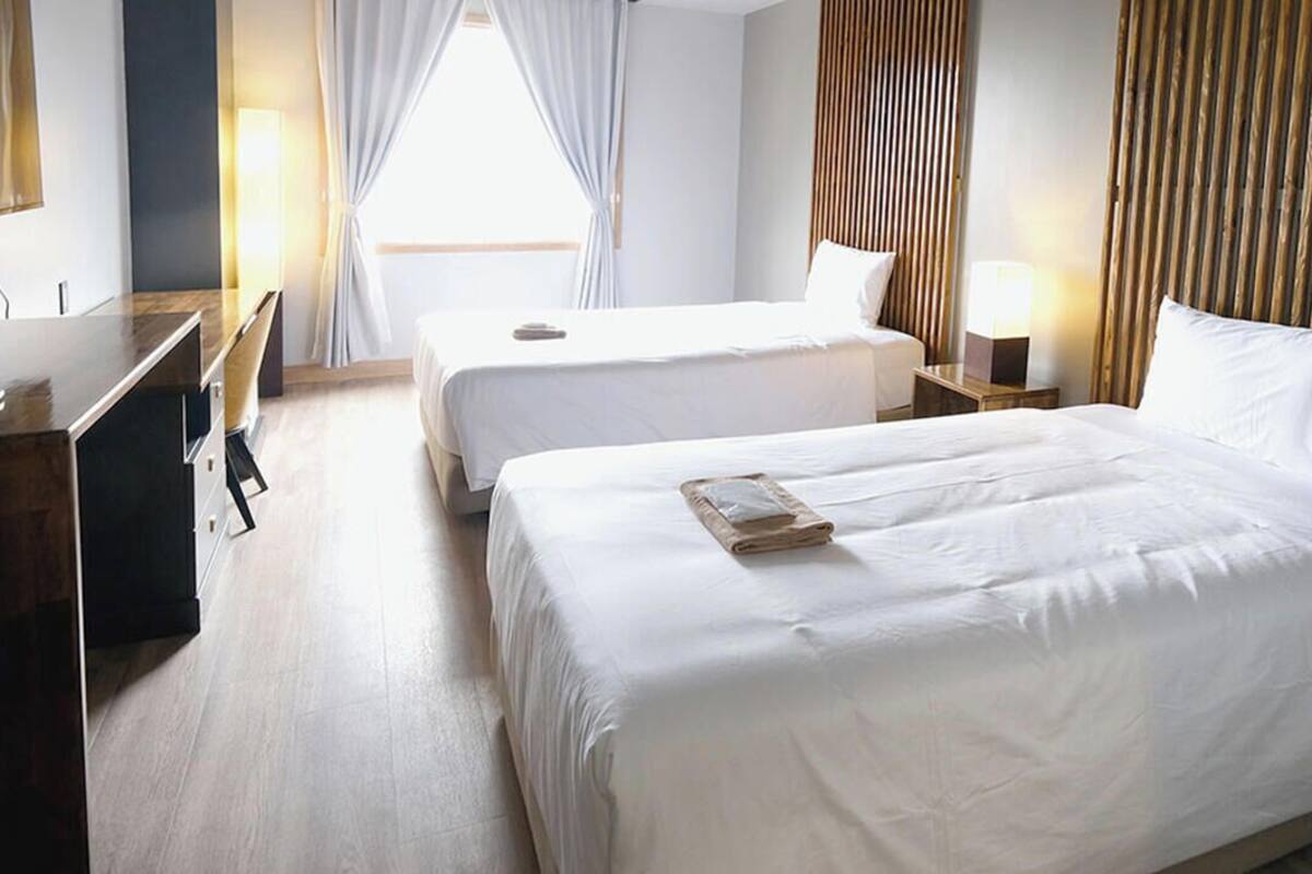 Una habitación de hotel con dos camas, un escritorio y un ventanal grande con cortinas.