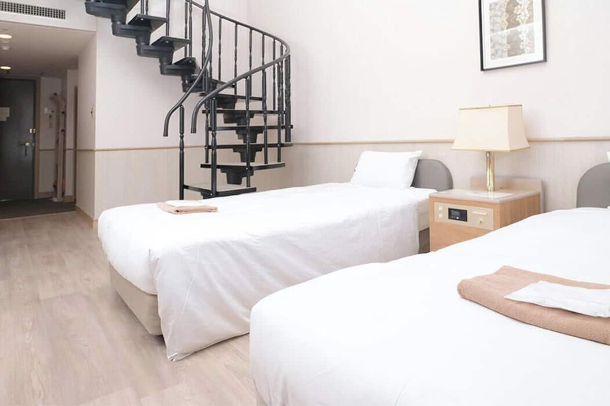 Habitación de hotel con dos camas, una escalera de caracol, una mesita de noche con lámpara y un cuadro enmarcado en la pared.