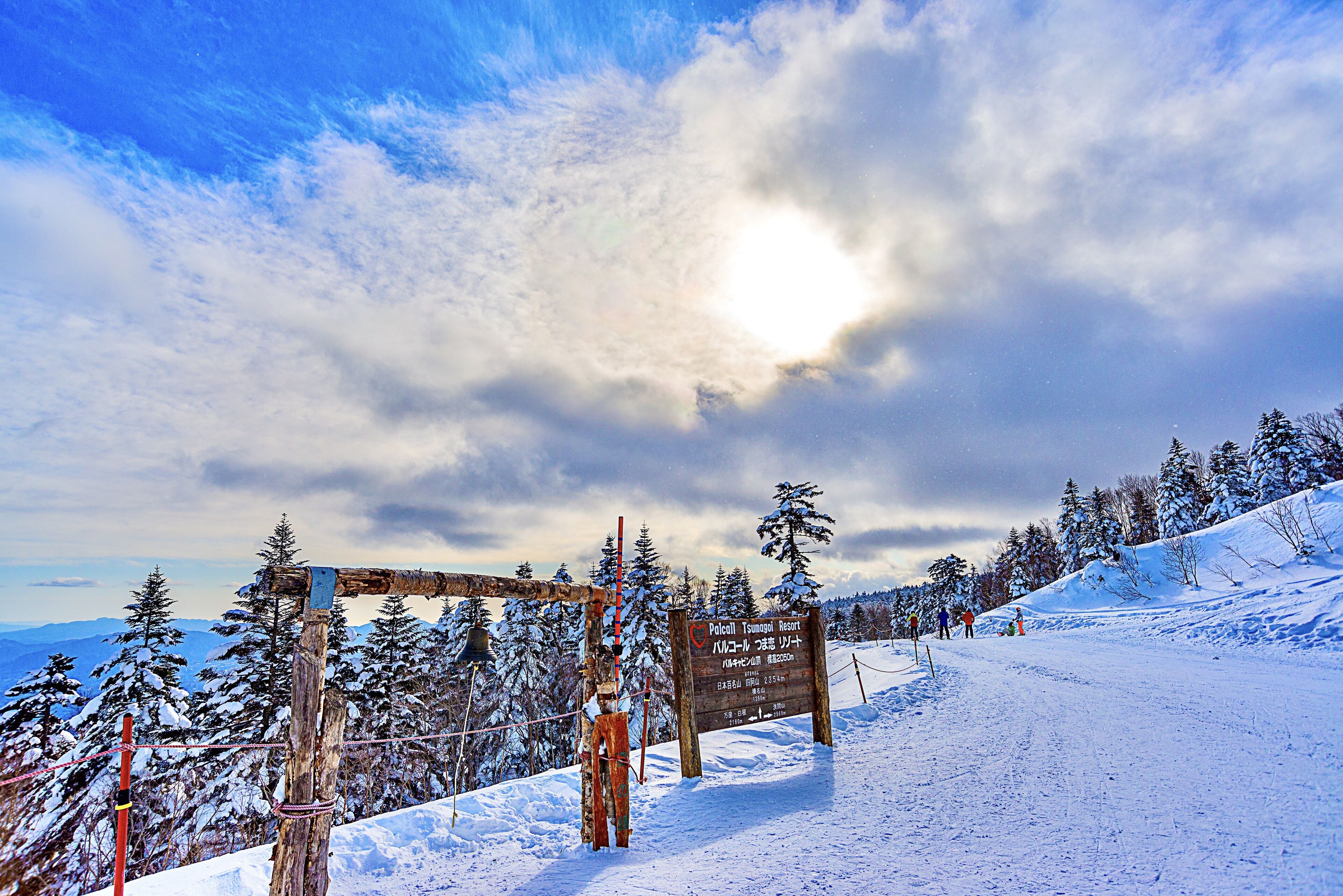 A snowy mountain landscape with a wooden signpost and a ski lift.