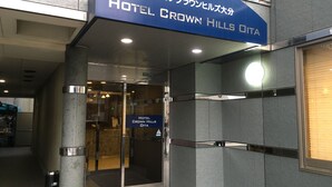 La entrada al Hotel Crown Hills Oita, con un diseño moderno, presenta una puerta de cristal y un letrero azul en la parte superior.