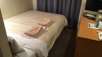 A hotel room with a bed, two towels, a desk with a phone, a monitor, and a coffee maker.