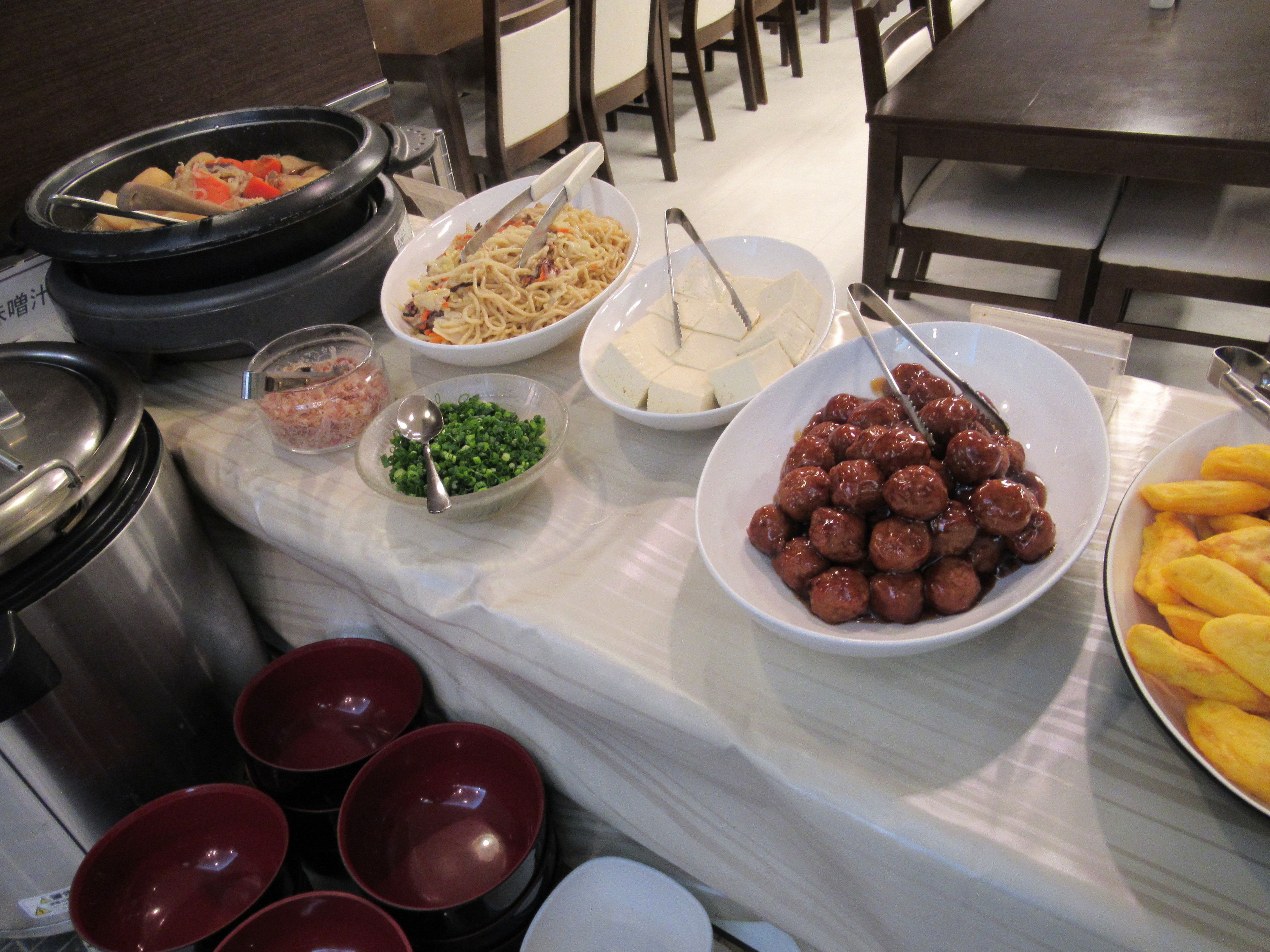 Una mesa de buffet con diversos platos, entre ellos fideos, albóndigas y verduras.