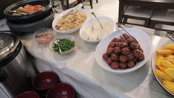Una mesa de buffet con diversos platos, entre ellos fideos, albóndigas y verduras.